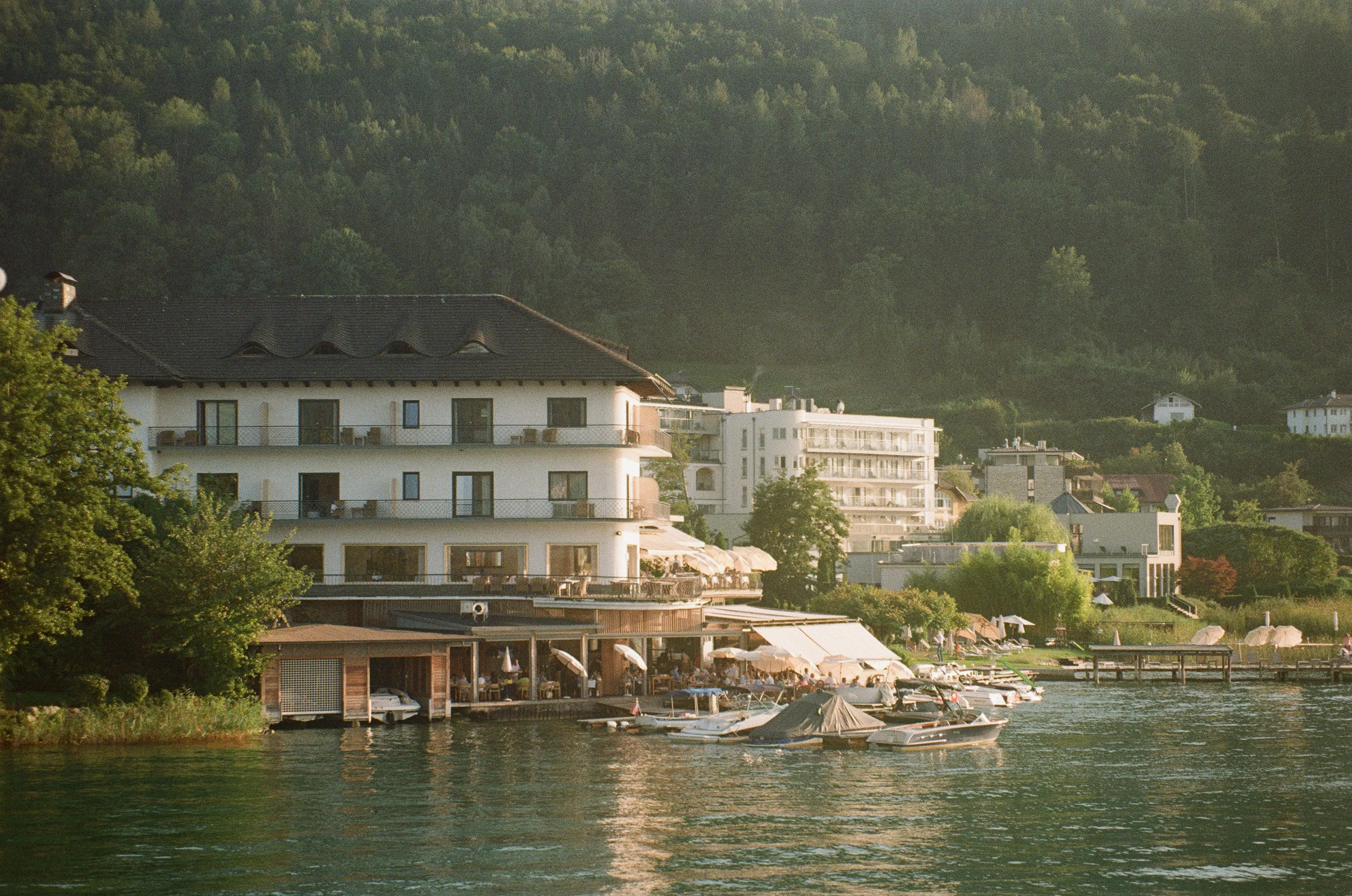 picture of a hotel with restaurant situated right on the edge of a lake, golden from the sun